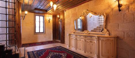A room with a wooden ceiling, a large ornate mirror, a patterned rug, and a light fixture on the wall.