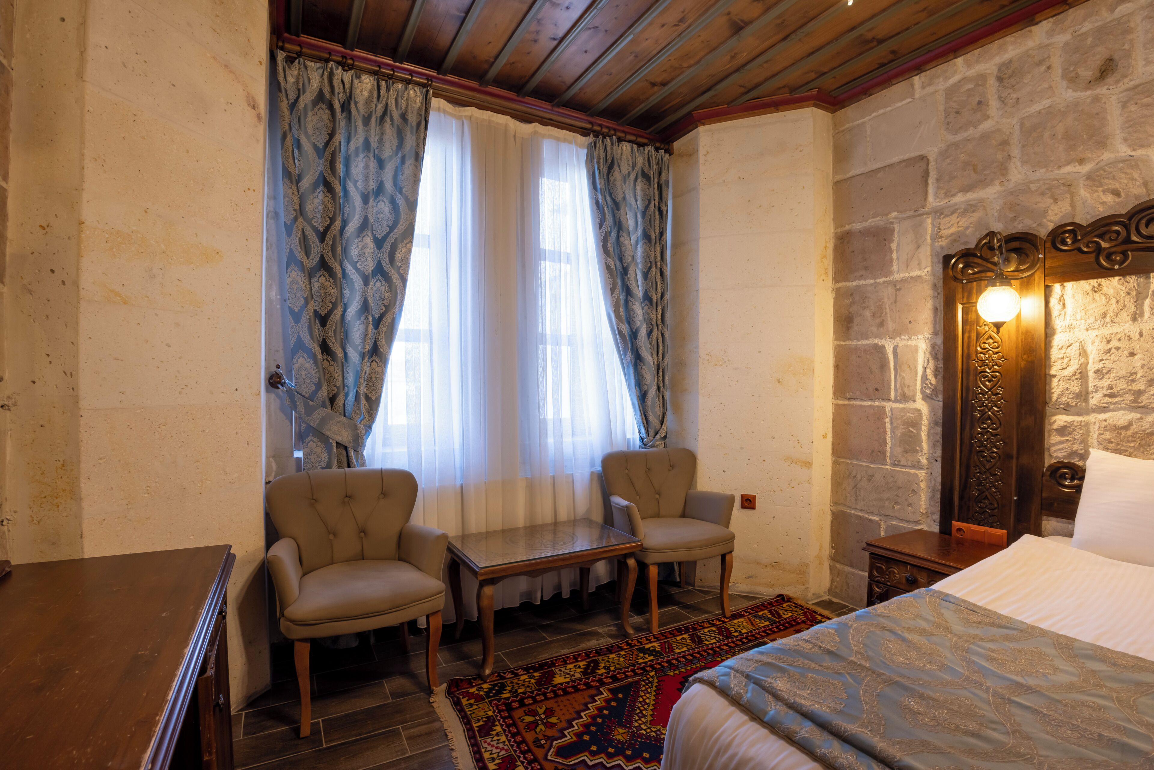 Una habitación con una cama, dos sillones, una mesita y un tapete estampado.