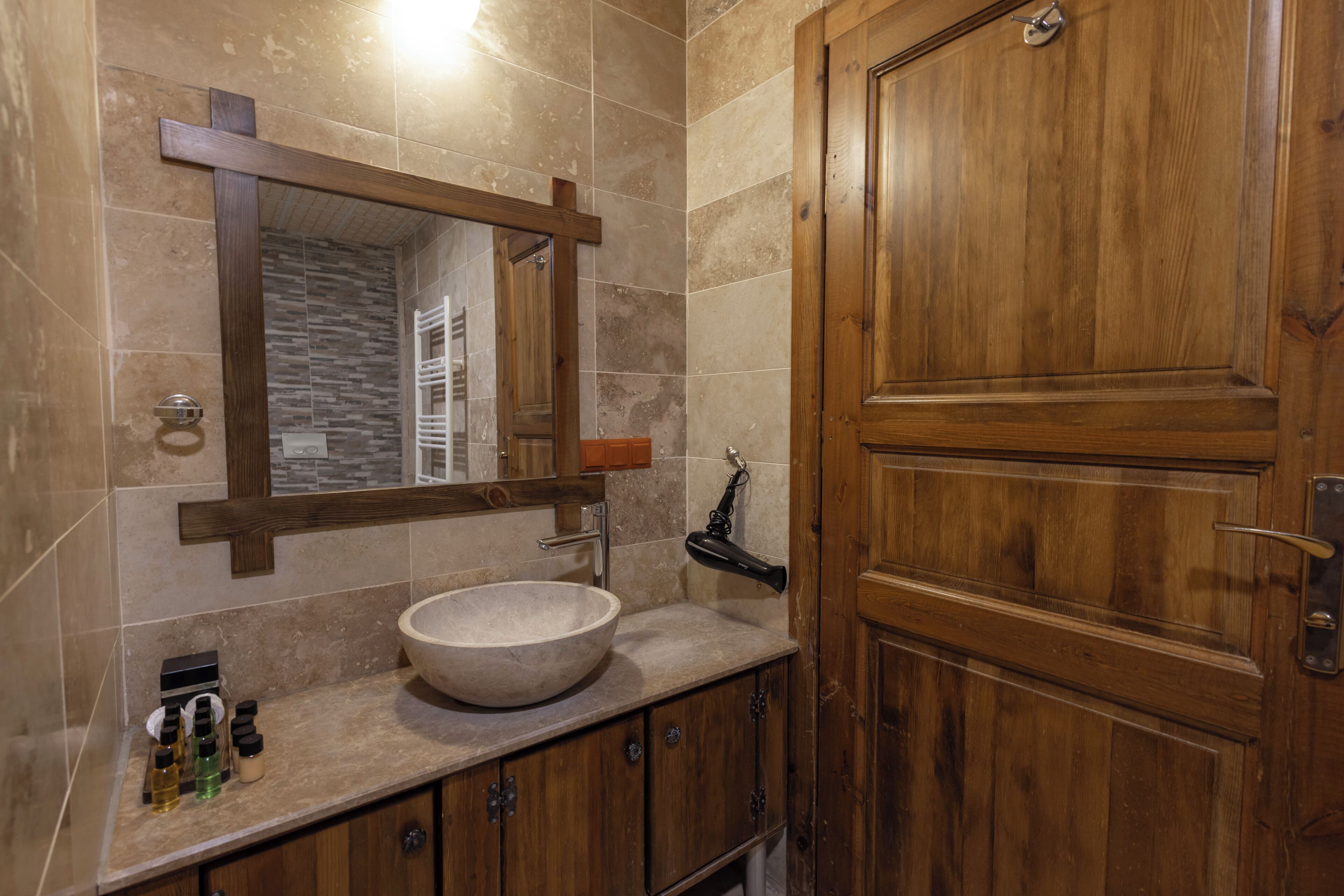 Une salle de bain avec une porte en bois, un grand miroir, un lavabo en pierre et un porte-serviettes.
