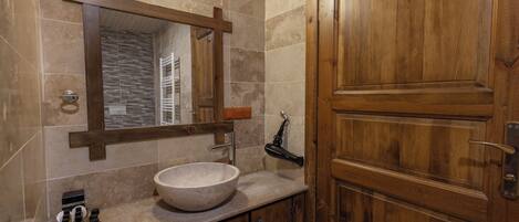 Une salle de bain avec une porte en bois, un grand miroir, un lavabo en pierre et un porte-serviettes.