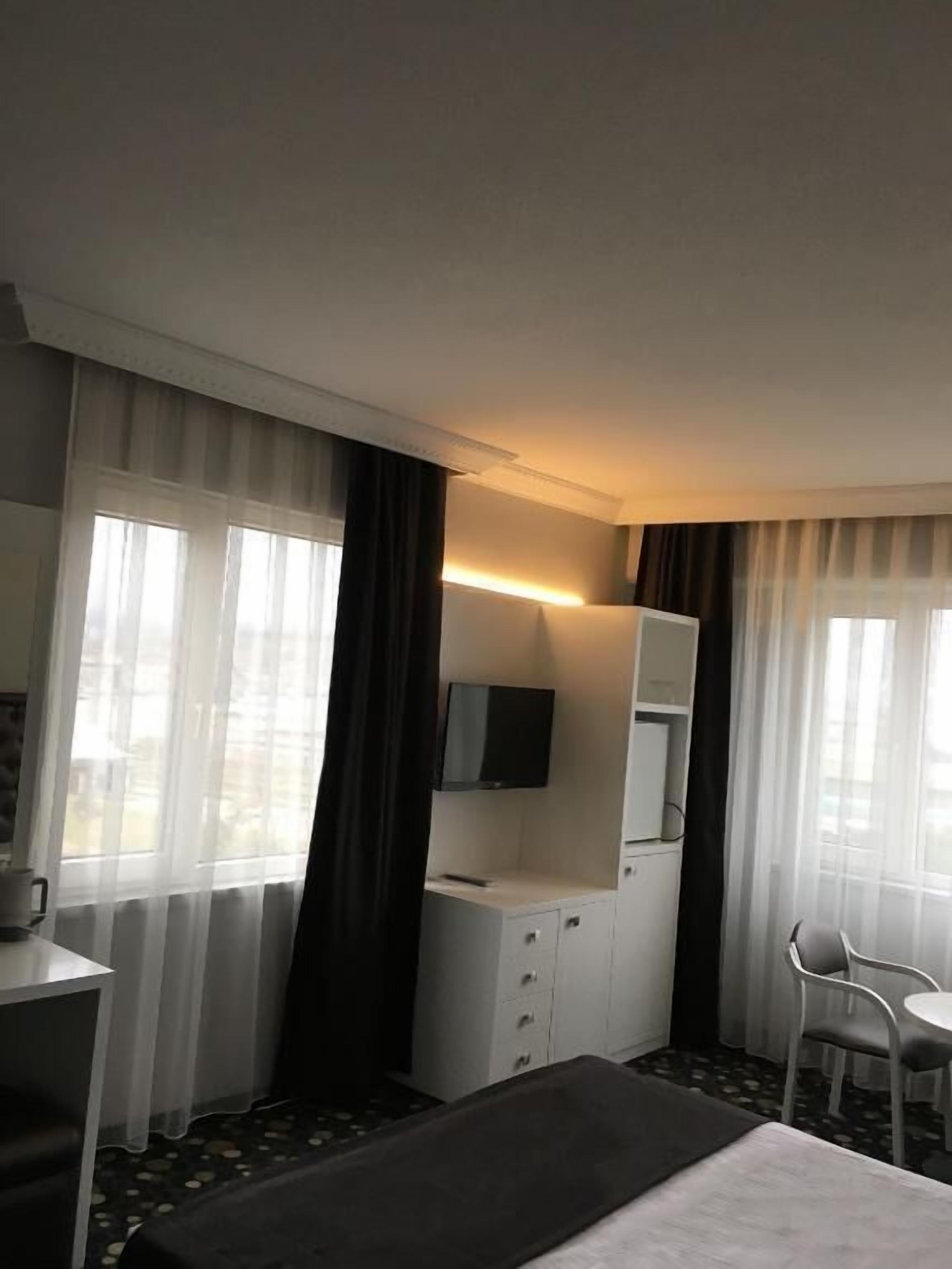 Habitación de hotel con cama, escritorio con silla, televisor montado en la pared y ventana con cortinas.