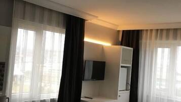 Habitación de hotel con cama, escritorio con silla, televisor montado en la pared y ventana con cortinas.