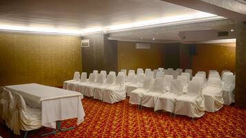 Un salón de conferencias con filas de sillas blancas y una mesa, cubierto por alfombra roja con diseño dorado.