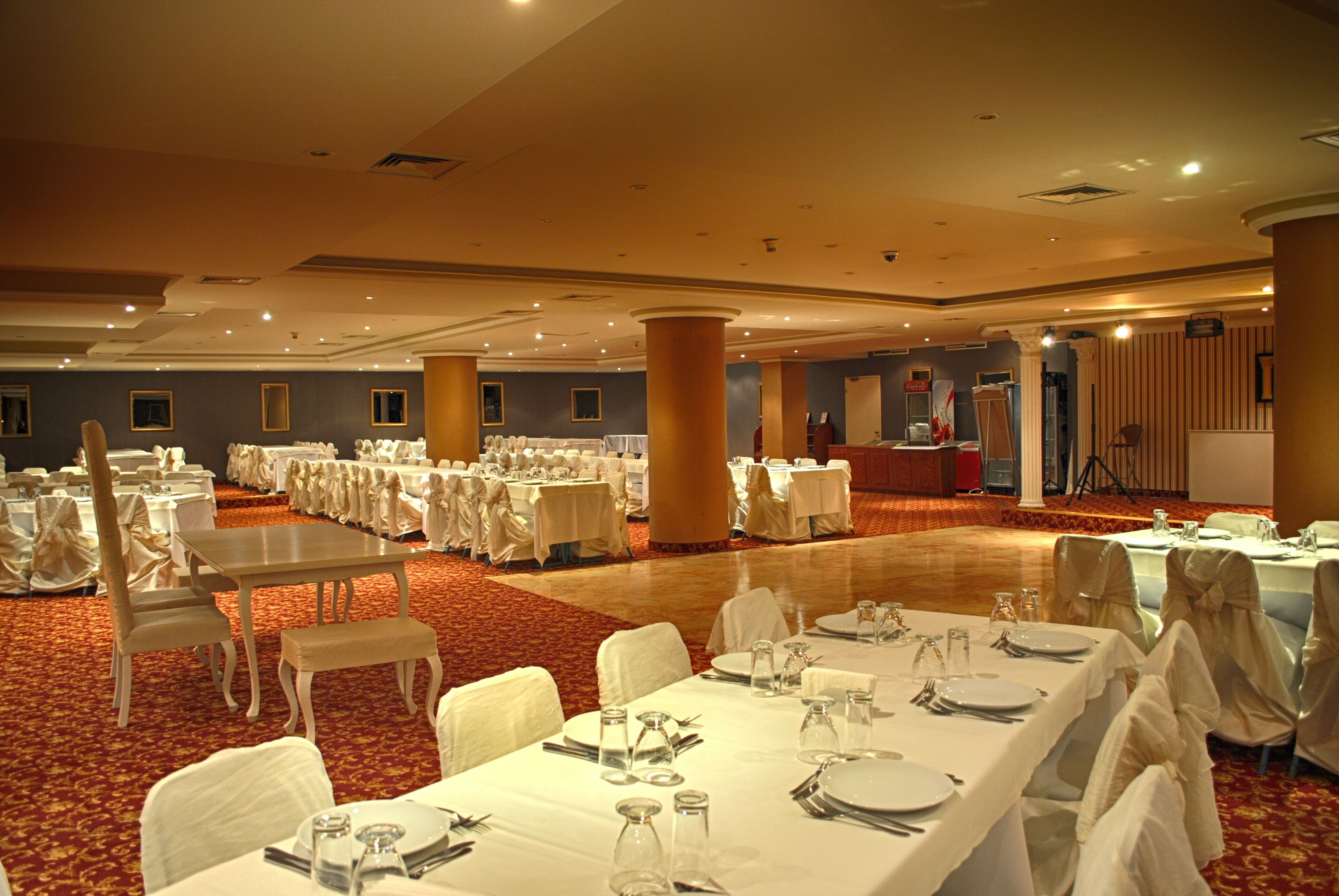 A banquet hall with multiple round tables set for dining, white chairs, and a carpeted floor.