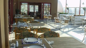 A sunlit outdoor dining area with tables and chairs, a covered walkway, and a view of the interior. - Hotel Eken Prestige (Bandirma)
