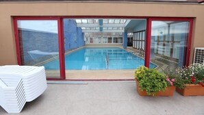 A rooftop swimming pool with glass doors, a stack of white lounge chairs, and potted plants. - Hotel Eken Prestige (Bandirma)