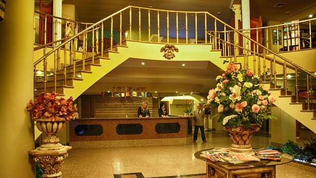 A hotel lobby with a reception desk, a grand staircase, and decorative vases. - Hotel Eken Prestige (Bandirma)