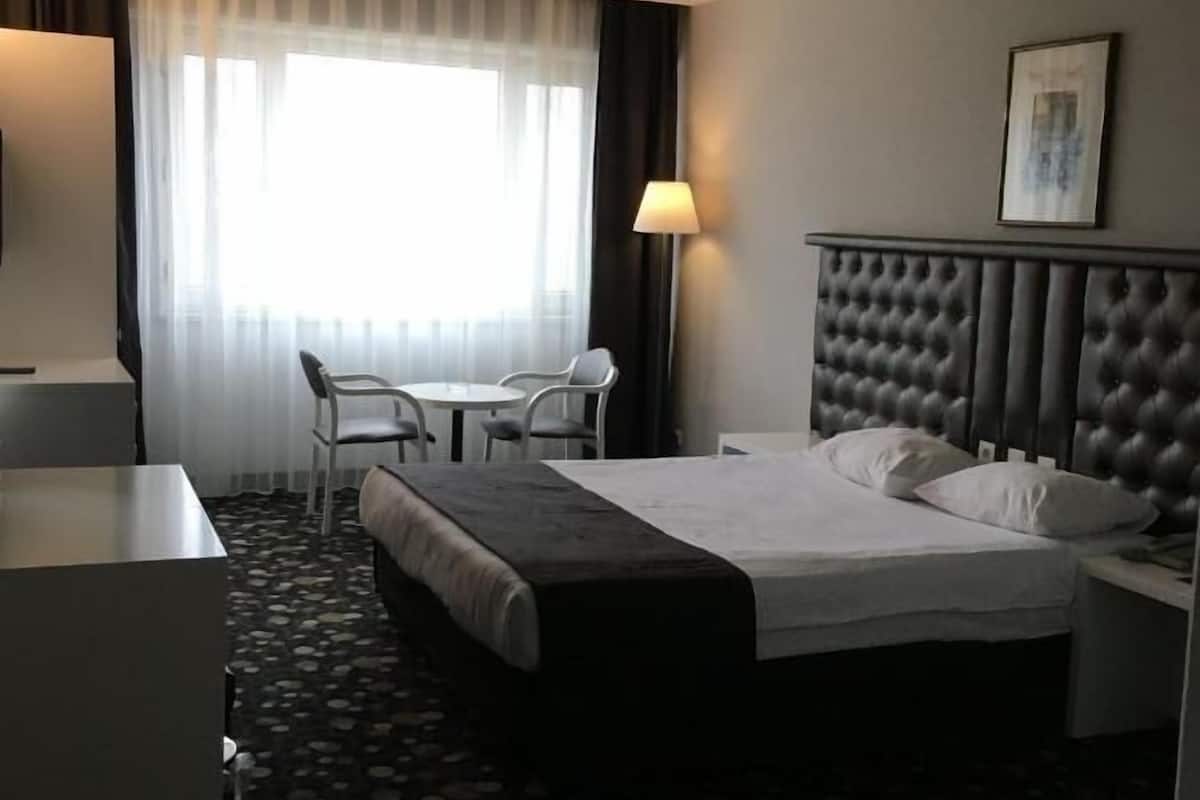 Una habitación de hotel con cama, escritorio, silla y una mesita.