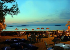 A seaside restaurant with outdoor seating, umbrellas, and a view of the sea and islands.