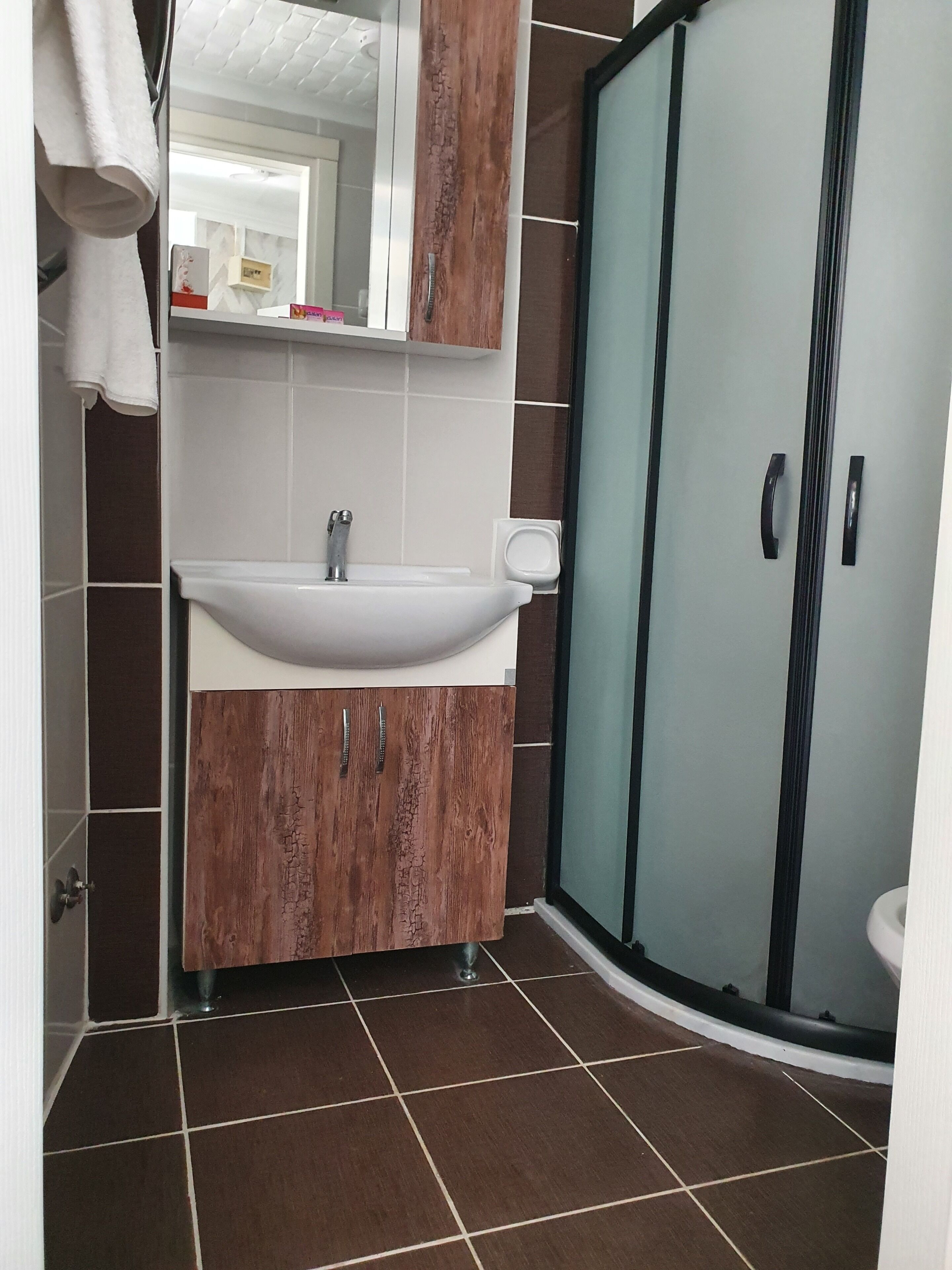 Un baño con lavamanos blanco, tocador de madera y cabina de ducha con mampara de vidrio.