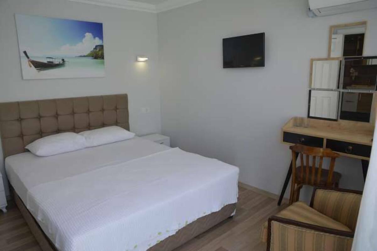 A bedroom with a bed, a desk, a chair, a television, and a painting on the wall.