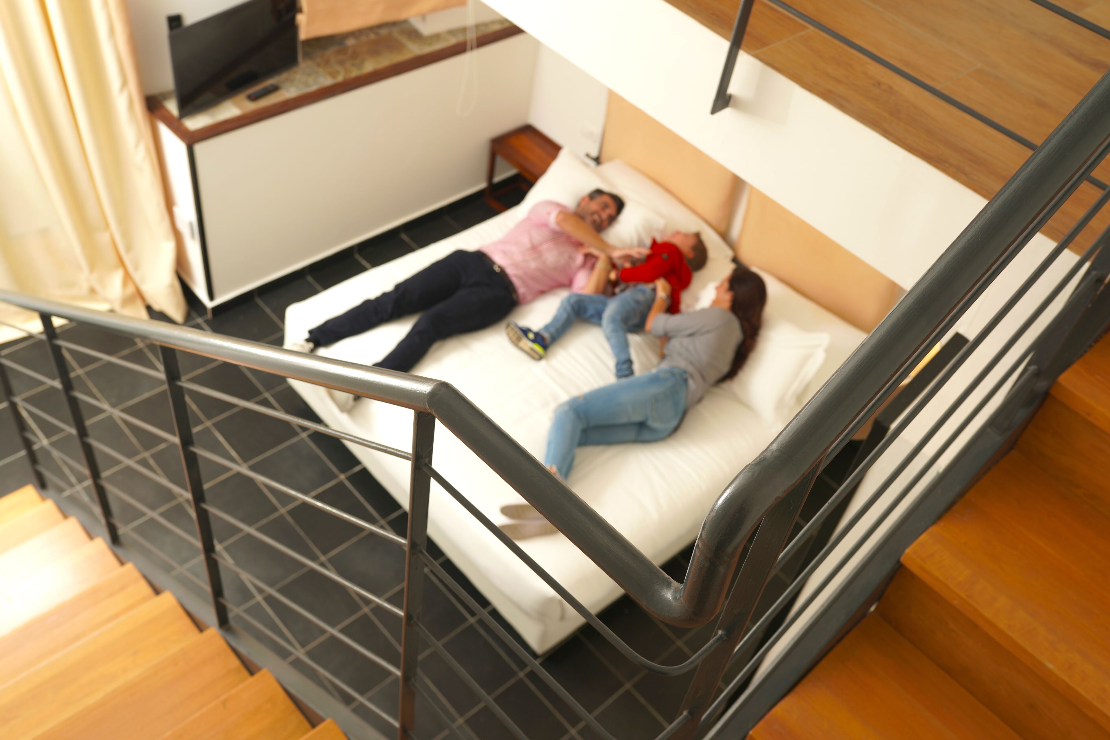 A bunk bed with two people lying on it, a TV on a stand, and a wooden floor.