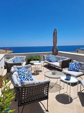 Una terraza con mobiliario exterior, incluyendo sofás y sillones, dispuestos alrededor de una mesa central.