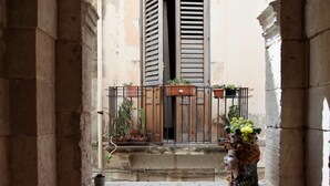 An arched doorway leading to a balcony with potted plants and a wooden door. - Lanterne Magiche Ortigia (Syracuse)
