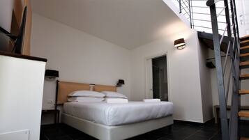 A modern bedroom with a large bed, a small bedside table, a wall-mounted lamp, and a staircase leading to an upper level.