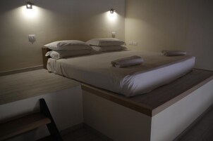 Un letto singolo con una testata in legno, due luci fissate al muro e una panca di legno ai piedi del letto.