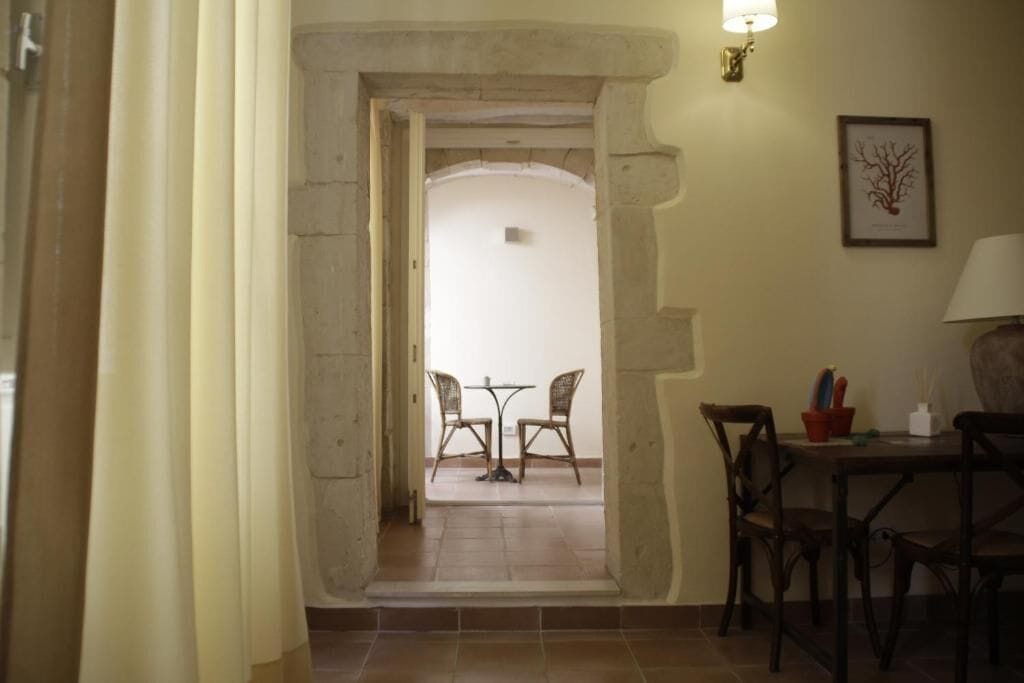 Un couloir étroit mène à un coin repas composé de deux chaises et d’une table, d’une lampe et d’un tableau encadré accroché au mur.