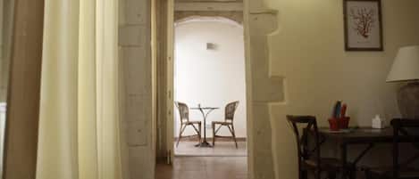 Un pasillo estrecho que conduce a un comedor con dos sillas y una mesa, una lámpara y un cuadro en la pared.