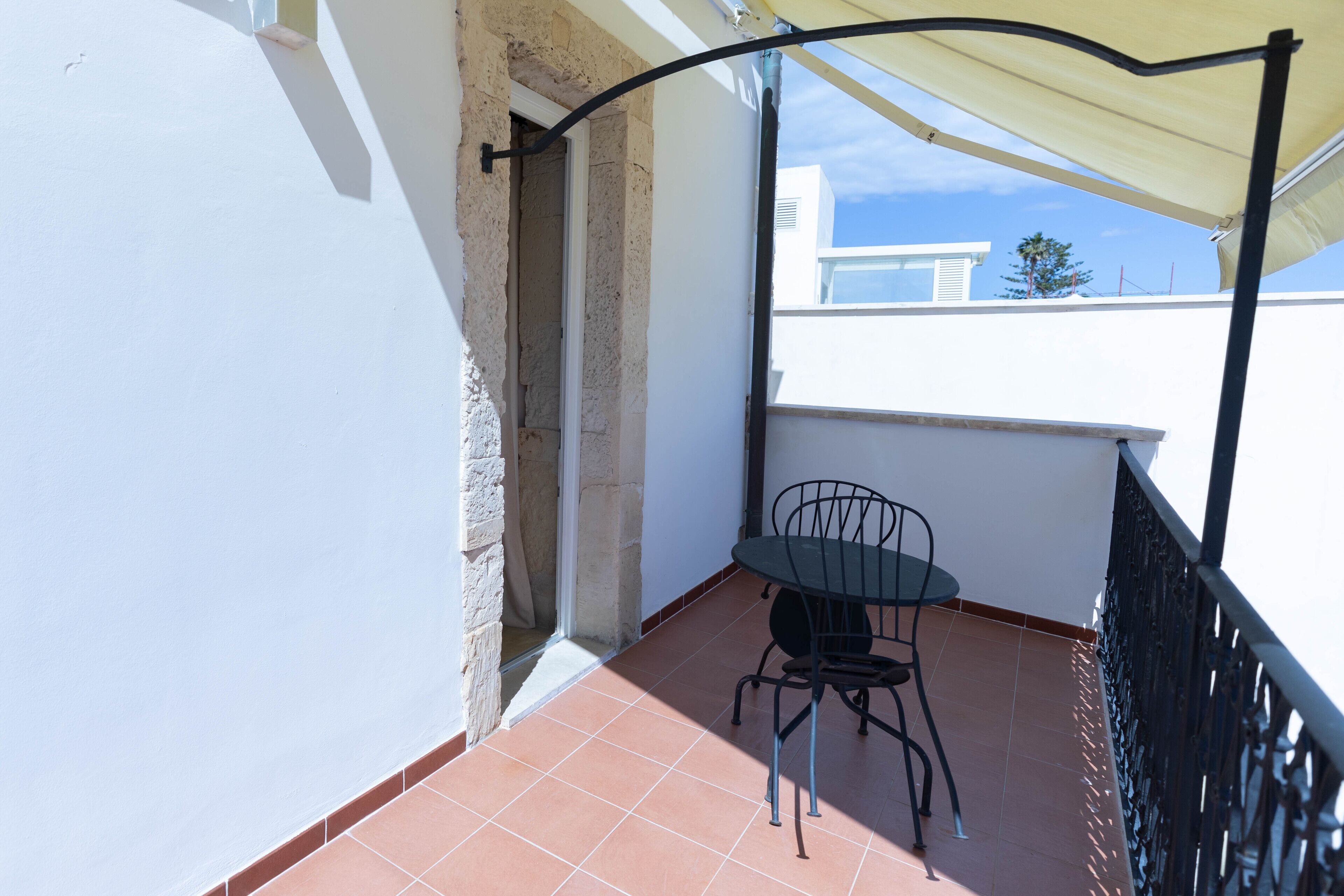 A balcony with a table and chair, a white wall, and a tiled floor.