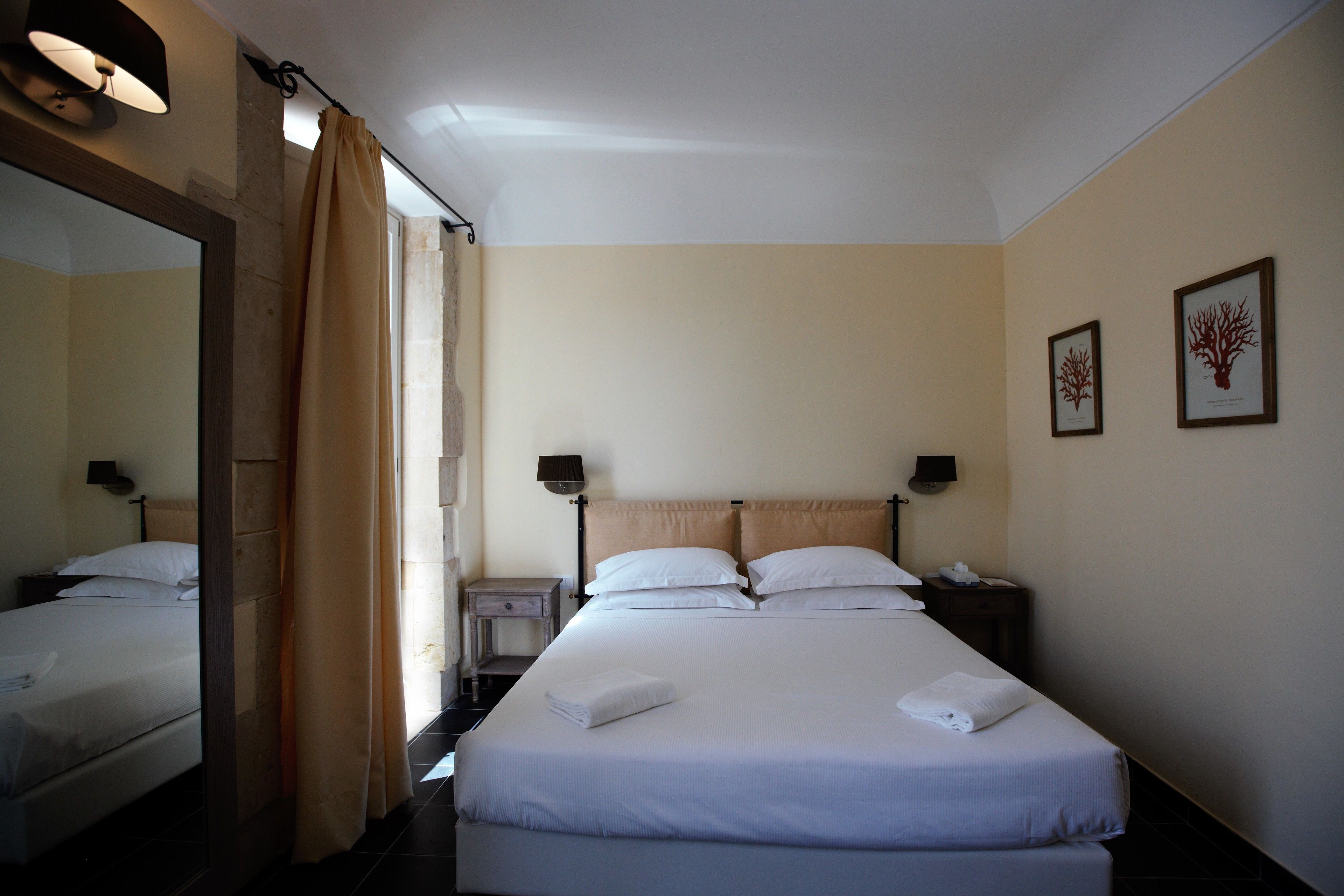 A hotel room with a large bed, bedside tables, a mirror, and two framed pictures on the wall.