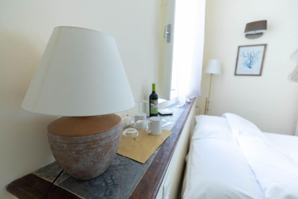 Ein Zimmer mit einem Bett, einem Nachttisch mit Lampe, einer Flasche und einer Tasse.