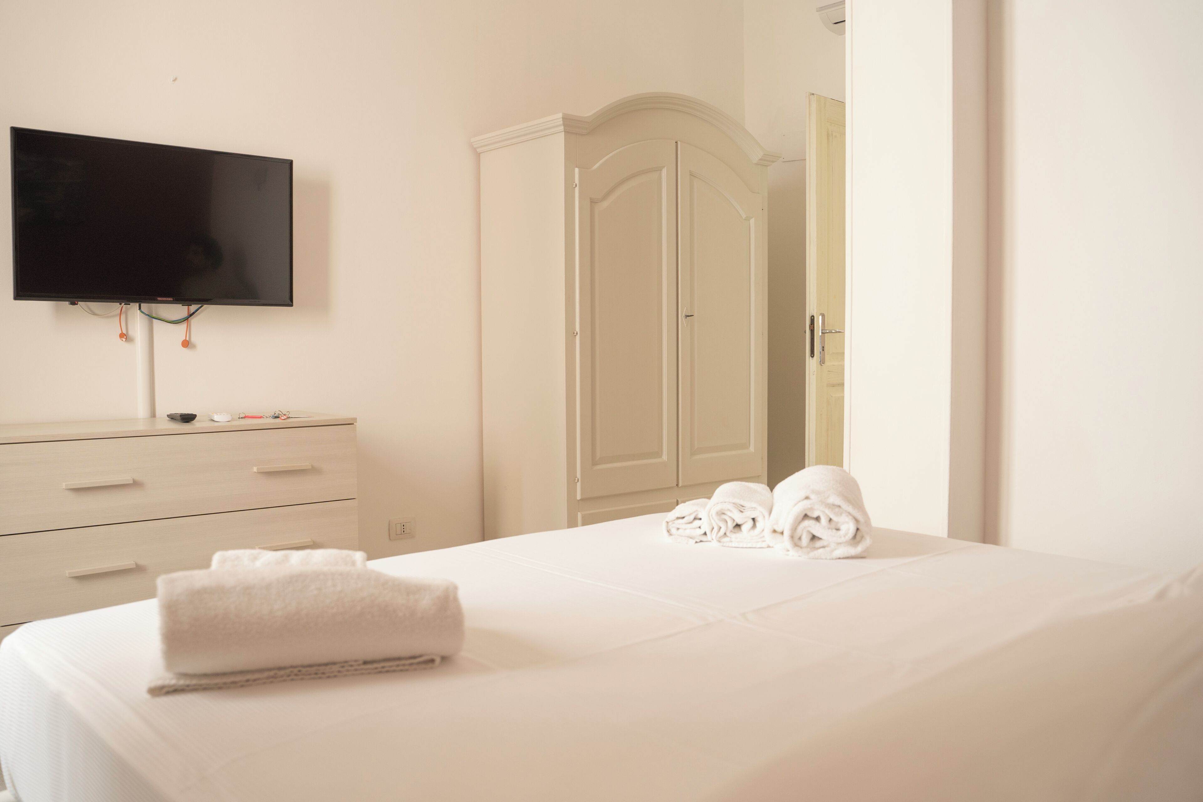 Ein Hotelzimmer mit Bett, Wandfernseher, Kleiderschrank und einer Tür zu einem anderen Raum.