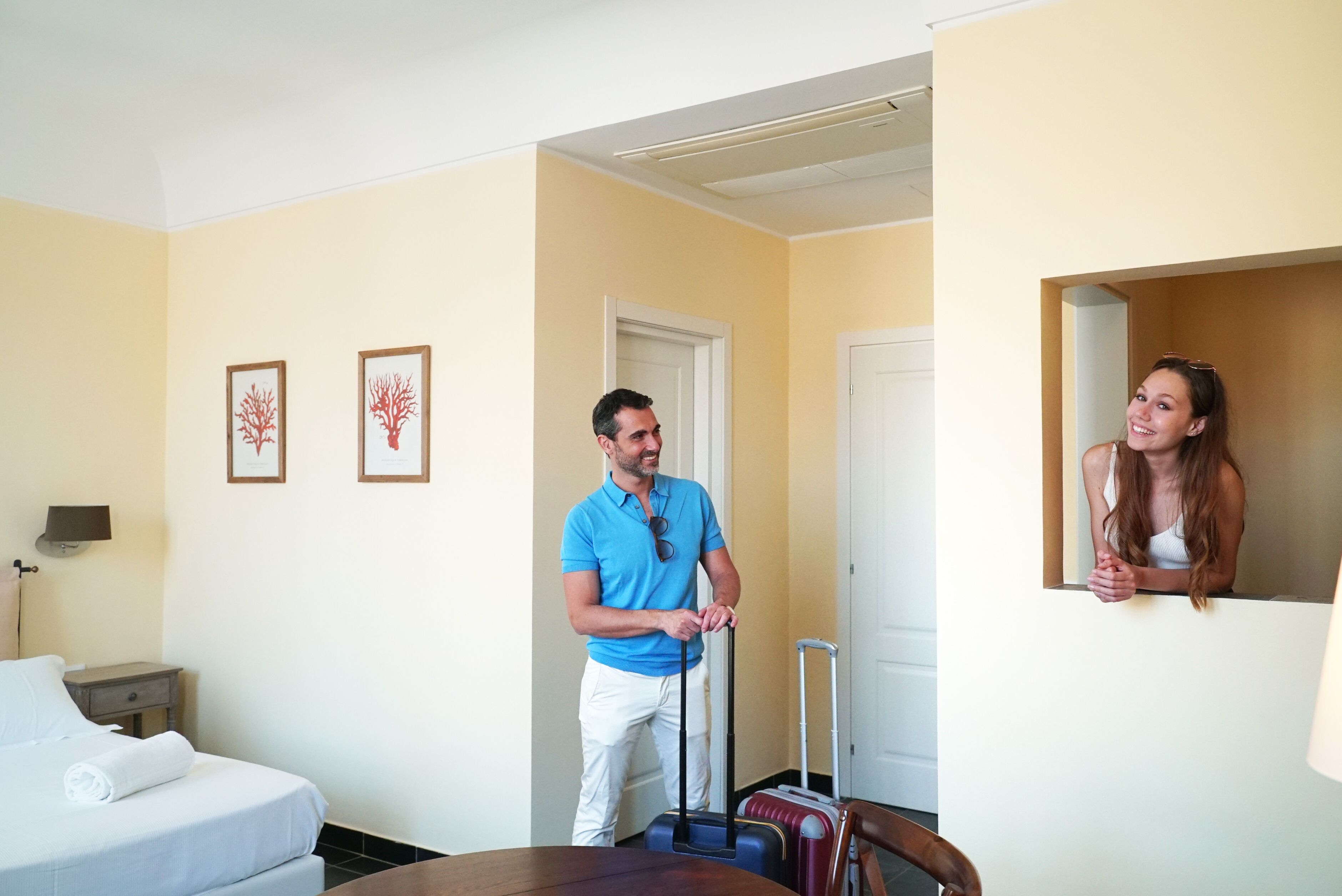A hotel room with a bed, a desk, a chair, a suitcase, and a mirror.