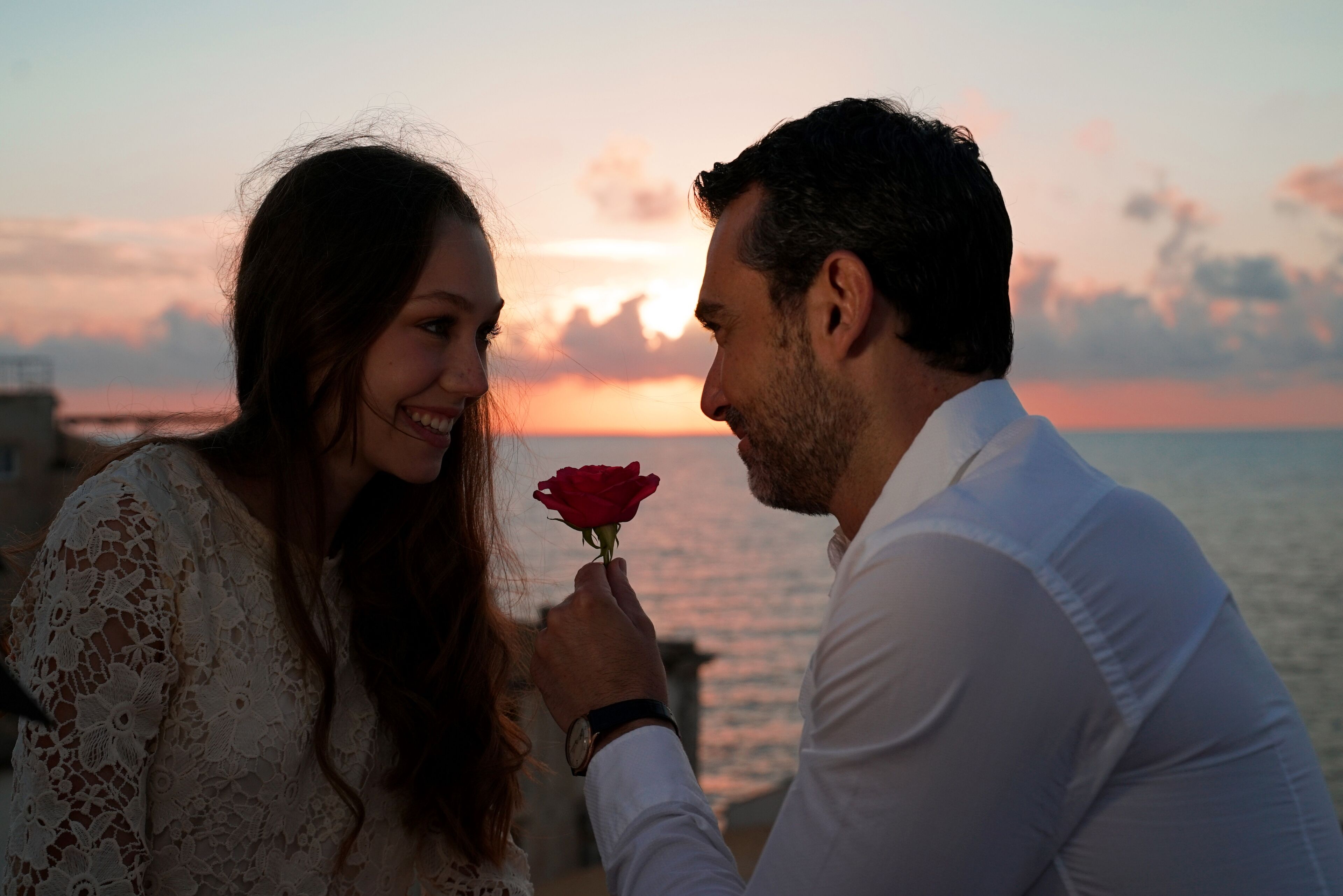 A couple holding a rose against a sunset backdrop.