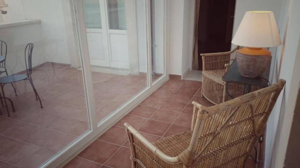 A balcony with wicker chairs, a table with a lamp, and a sliding glass door leading to a patio area.