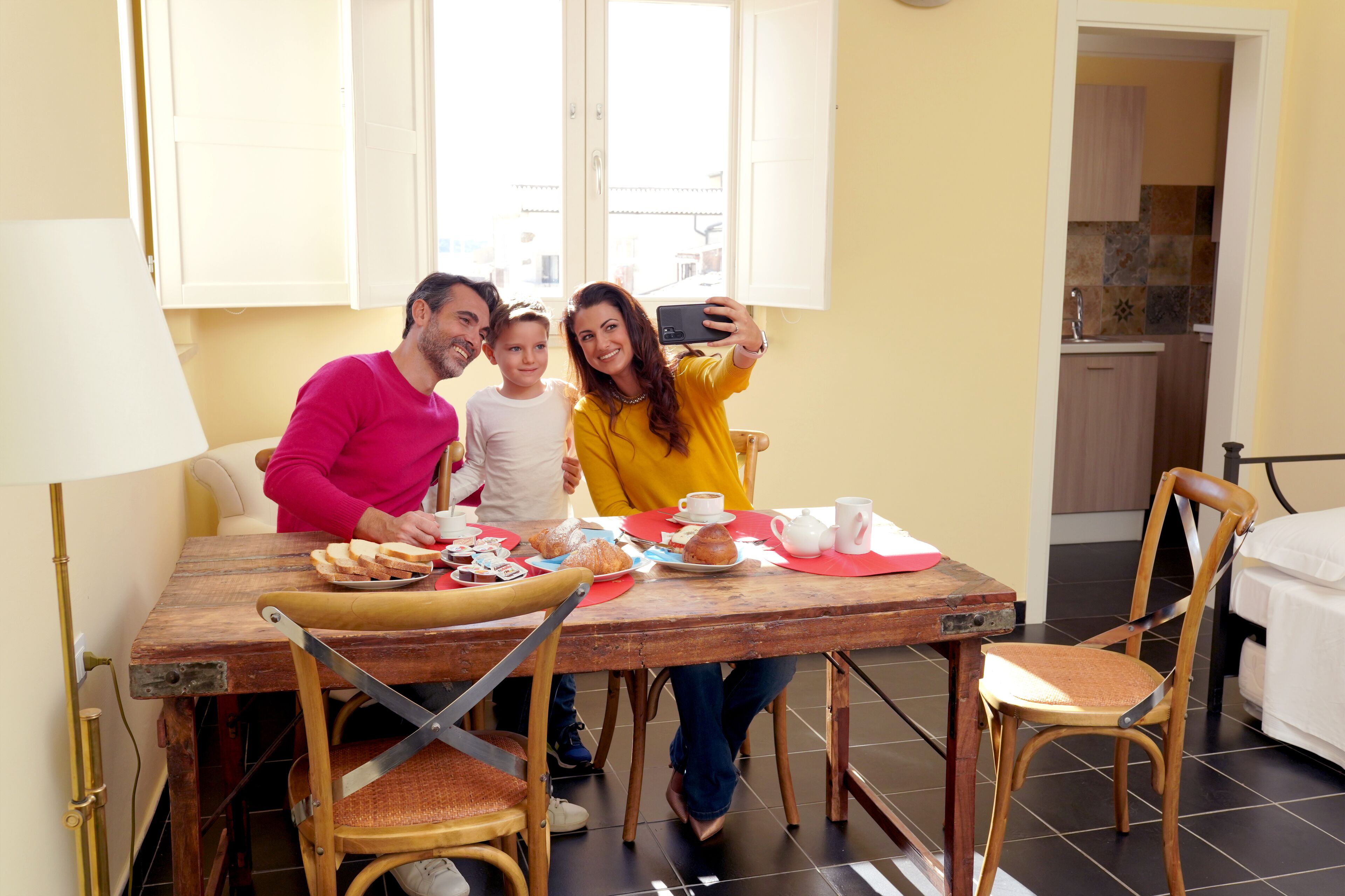 Un coin repas avec une table en bois, des chaises et une table préparée pour le petit-déjeuner, avec des viennoiseries et des tasses.