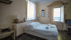 A hotel room with a bed, a desk with a lamp, a television, and a window with curtains. - Lanterne Magiche Ortigia (Syracuse)