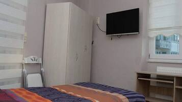 Un dormitorio con cama, armario, televisor y ventana con persianas.
