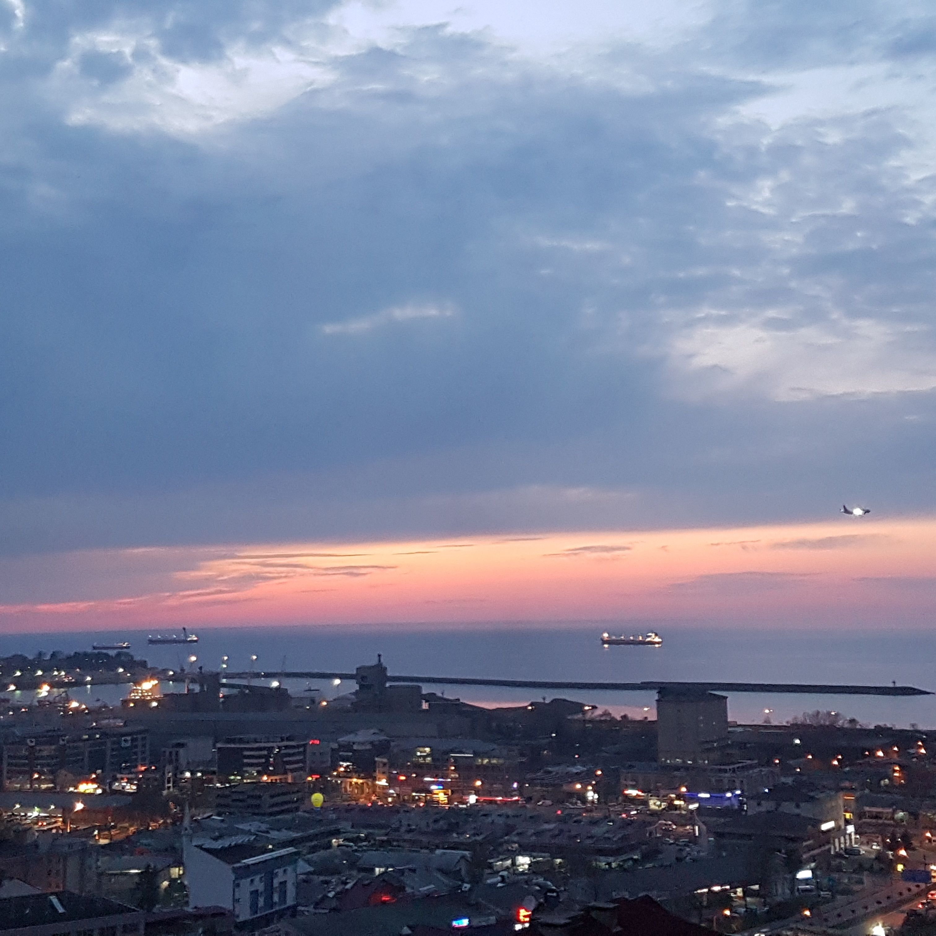 A cityscape at dusk with a view of the waterfront, buildings, and a bridge.