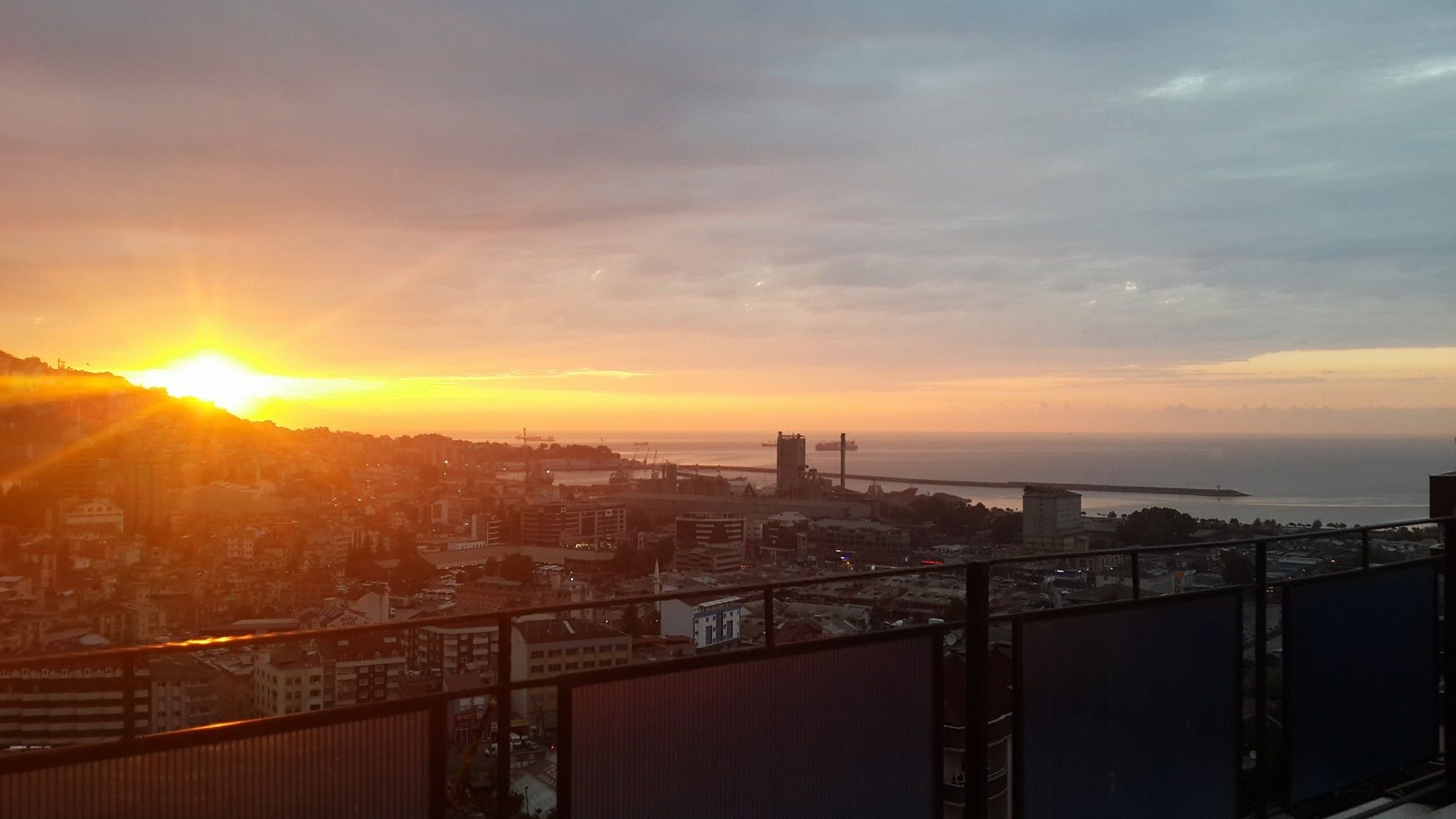 Vista urbana ao pôr do sol, com o mar e uma ponte.