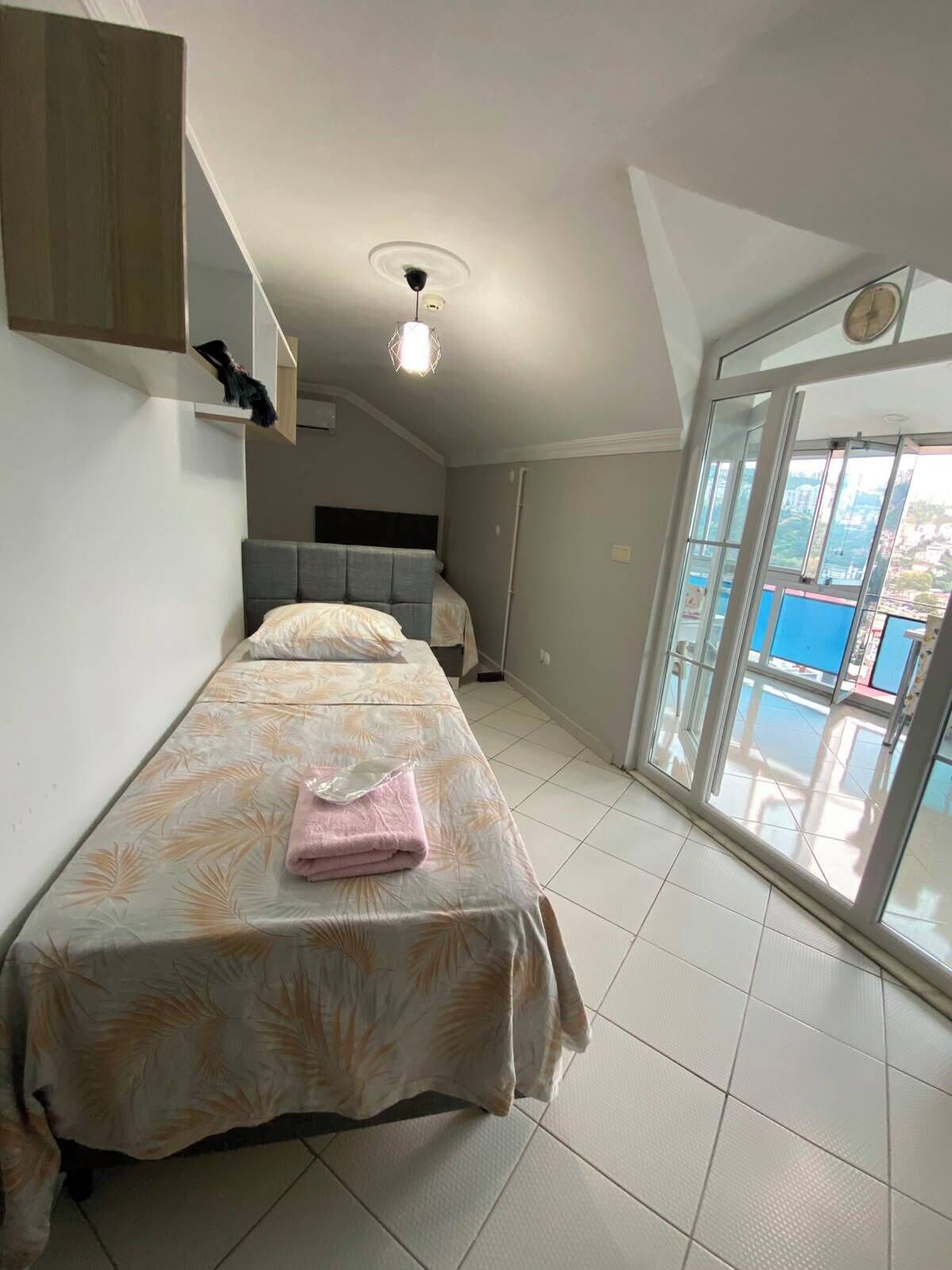 A bedroom with a bed, a nightstand, a ceiling light, and a view through a glass door.