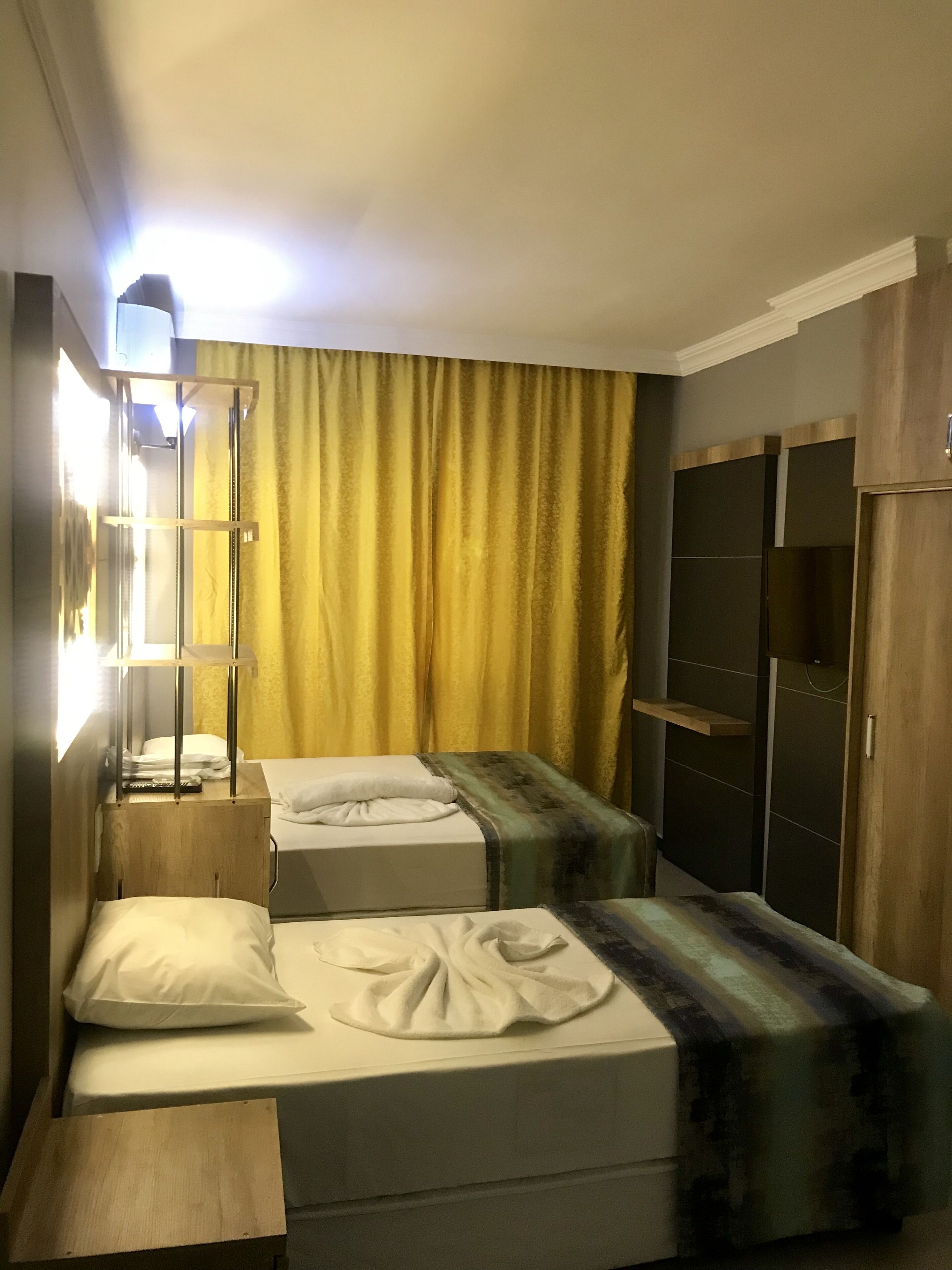 A hotel room with two single beds, a wooden nightstand, a mirror, and a wardrobe.