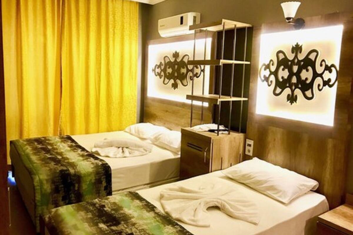 A hotel room with two beds, a wooden headboard, a bedside table, a nightstand, and a wall-mounted shelf.