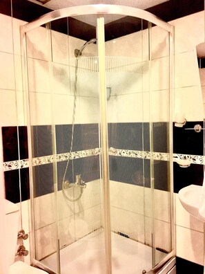 A glass-enclosed shower with a curved ceiling, a handheld showerhead, and a white sink with a faucet to the right. - Otel Star Palace (Antalya)