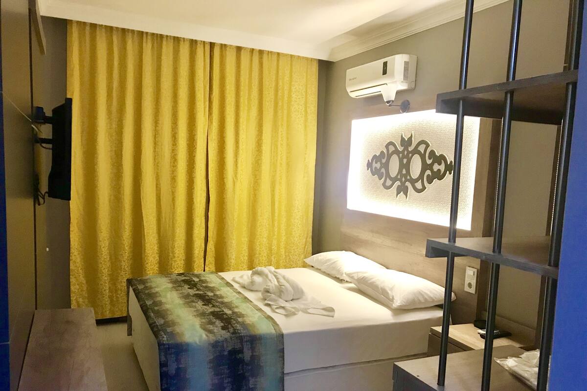 A hotel room with a bed, a window with a decorative pattern, an air conditioning unit, and a curtain.