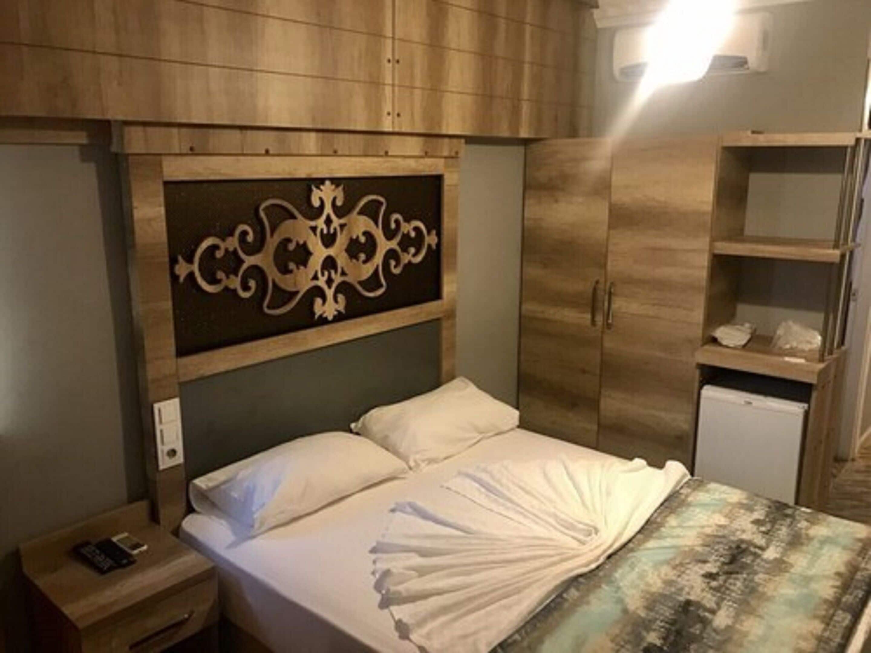 A hotel room with a bed, a nightstand, a wardrobe, and a small desk.