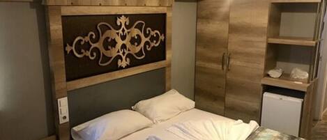 A hotel room with a bed, a nightstand, a wardrobe, and a small desk.