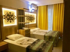 A hotel room with two beds, a nightstand, a wall-mounted shelf, and a window with yellow curtains. - Otel Star Palace (Antalya)