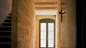 Un couloir avec un escalier sur la gauche, une porte ornée d’une croix sur le mur à droite, et un tapis rouge menant à la porte.