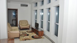 Un salon avec un canapé beige, un fauteuil en cuir, un téléviseur posé sur un meuble en bois et un tapis à motifs.