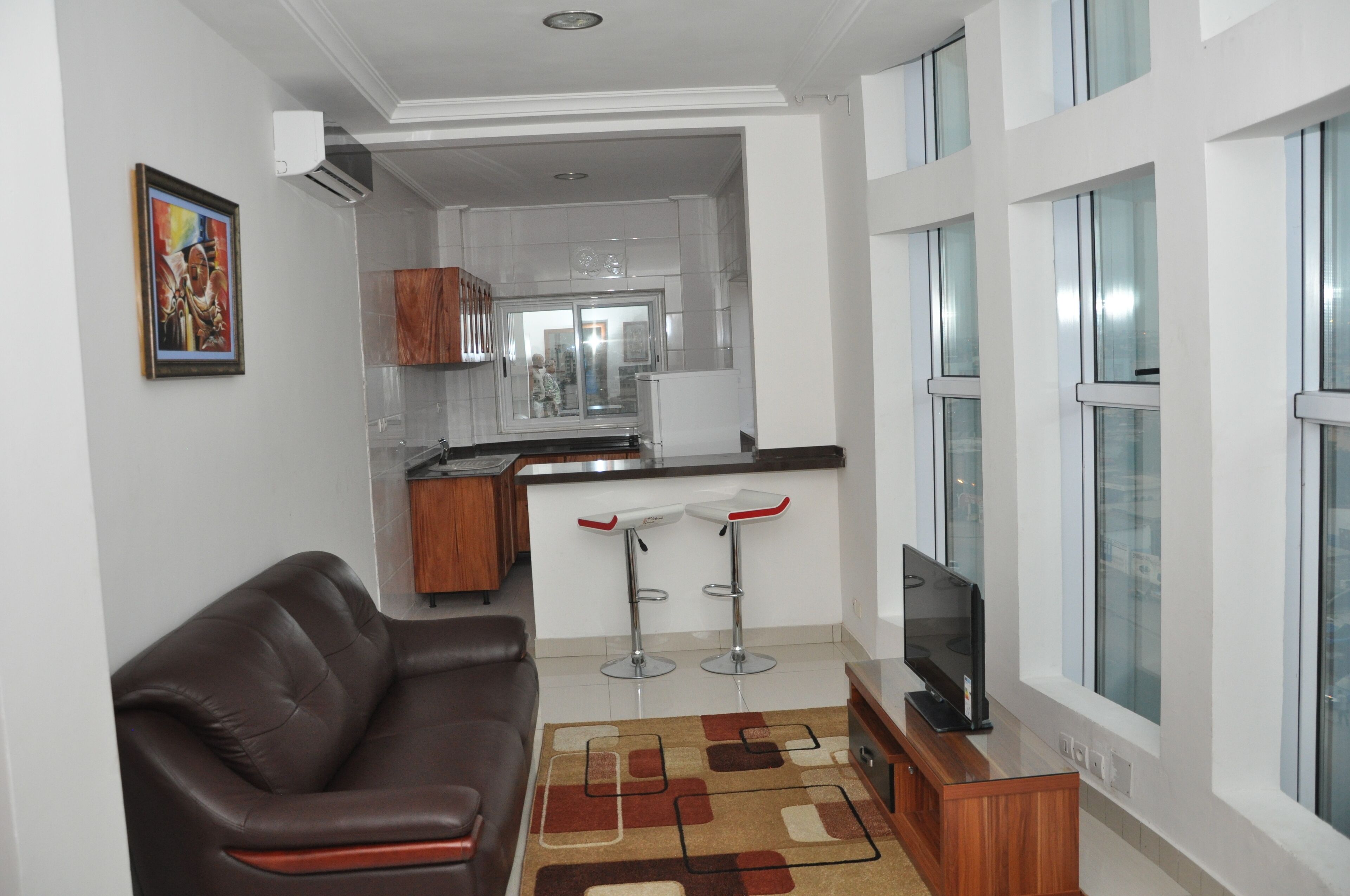 A modern living room with a brown leather sofa, a TV, and a kitchen area in the background.