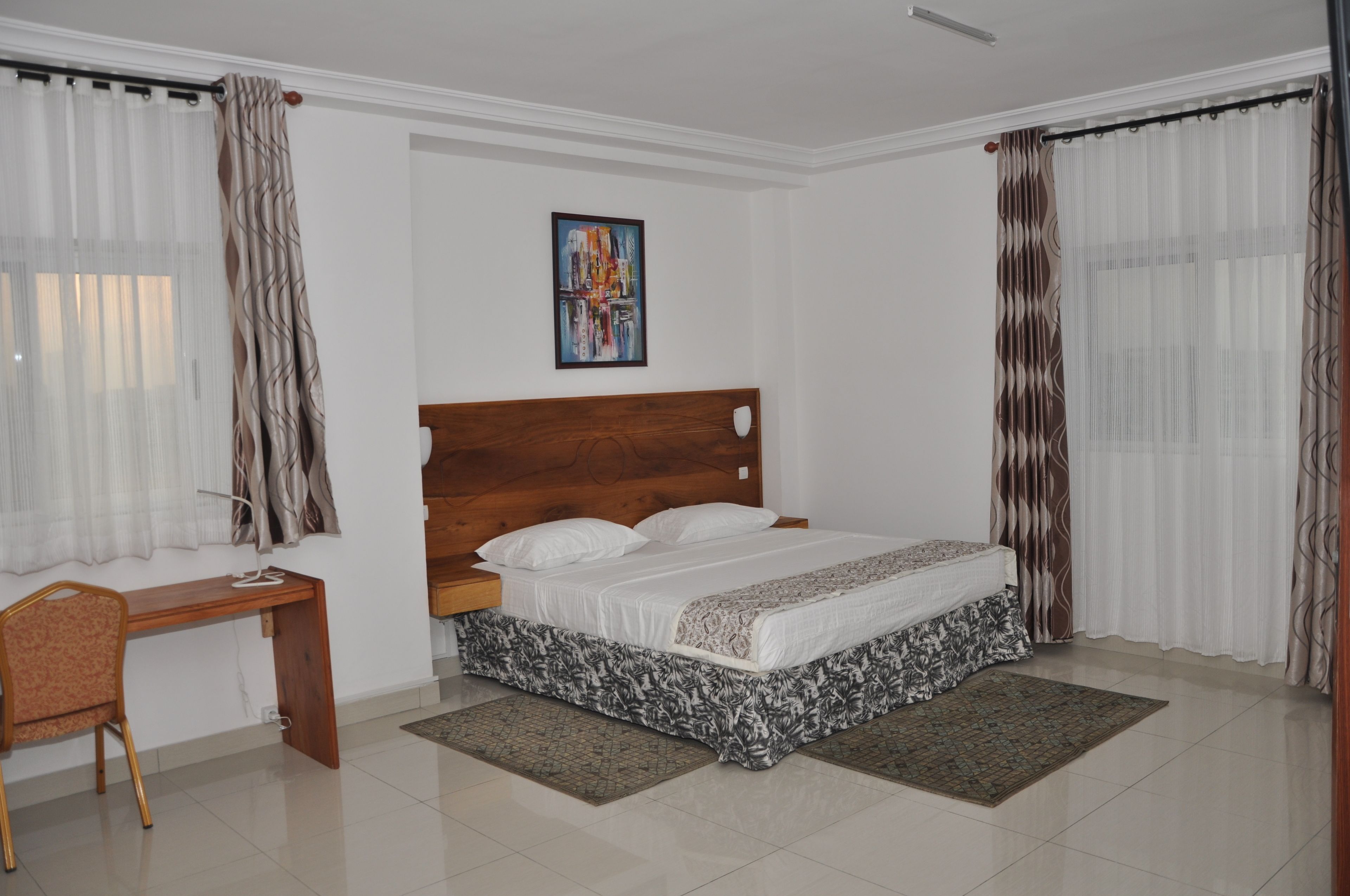 A bedroom with a wooden headboard, a bed with white bedding, a desk with a chair, and a painting on the wall.