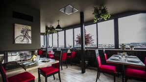 A restaurant with red chairs, a wooden table, and a view of the city through large windows.