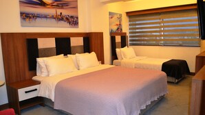 A hotel room with a large bed, a smaller bed, a nightstand, a drawer, and a window with blinds.
