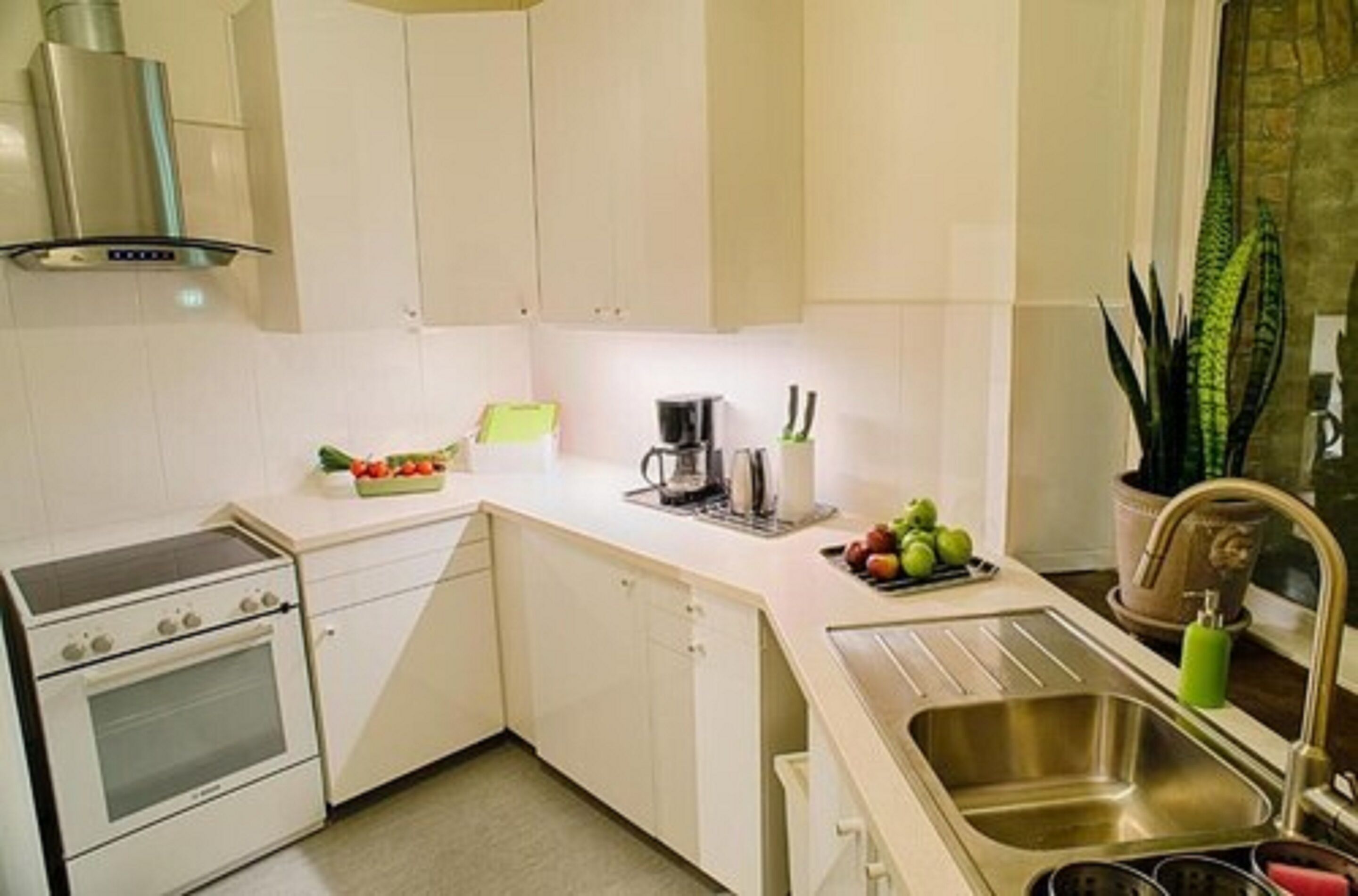 A compact kitchen with white cabinets, a stainless steel sink, and a stove.