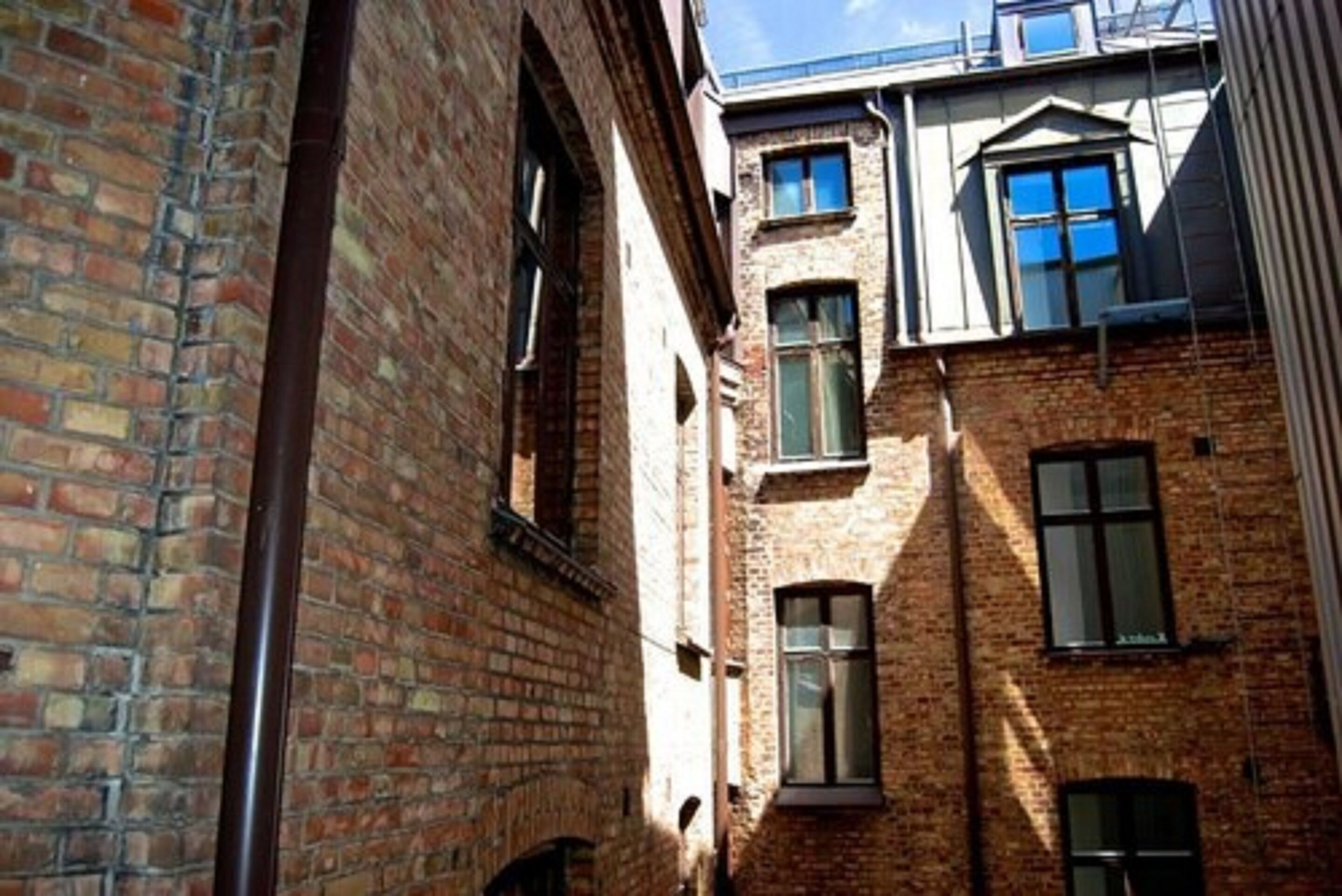 A narrow alleyway between two brick buildings with multiple windows and a visible chimney.